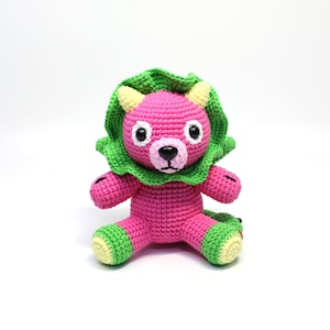 May include: A pink crocheted stuffed animal with green ears and a green collar. The animal has black eyes and a black nose.