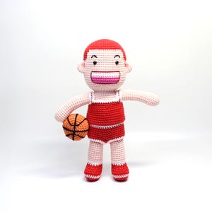 Puede incluir: Un jugador de baloncesto de crochet que lleva un uniforme rojo y blanco y sostiene un balón de baloncesto naranja.