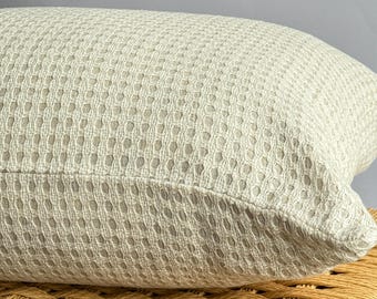 Könnte beinhalten: Nahaufnahme eines hellbeigen, strukturierten Kissens mit einem gewebten Muster. Das Kissen ist rechteckig und wirkt weich und liegt auf einer gewebten Oberfläche. Die neutrale Farbe und Textur deuten auf Komfort und Heimdekoration hin.