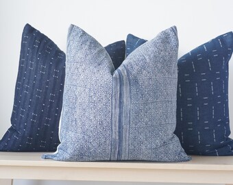 May include: Three blue and white patterned throw pillows with different designs. The pillows are arranged on a light wood surface.