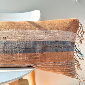 May include: A brown and blue striped throw pillow with fringe. The pillow is made of a woven fabric and has a soft, textured feel.