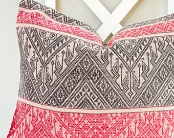 May include: A pink and gray patterned throw pillow with a geometric design. The pillow is sitting on a white chair.