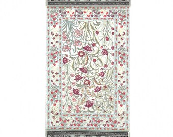 May include: A silver wall hanging with a blue evil eye charm. The wall hanging features a small tapestry with a floral pattern in shades of red, white, and green.