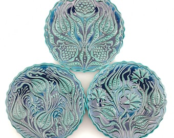 May include: Three round ceramic plates with a blue and green glaze. The plates feature a raised design of stylized flowers and leaves.