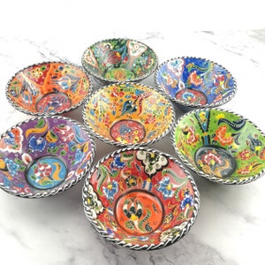 May include: Set of six colourful ceramic bowls with intricate floral patterns. Each bowl features a different colour scheme and design, with a black and white trim around the rim.