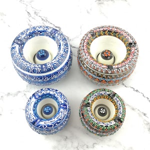 May include: Four ceramic ashtrays with intricate blue, white, orange, and green patterns. Each ashtray has a round, deep bowl with a small, round, white centre.