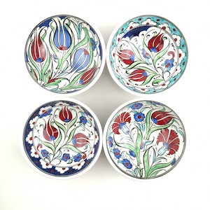 Può includere: Set di quattro piccole ciotole in ceramica con fondo bianco e intricati disegni floreali dipinti a mano in tonalità di blu, rosso e verde. Le ciotole presentano motivi tradizionali turchi di tulipani.