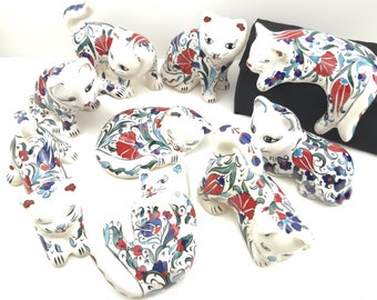 May include: A collection of nine ceramic cat figurines, each painted with intricate floral designs in shades of red, blue, and green on a white background.