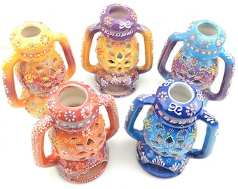 May include: Five colorful ceramic candle holders with intricate designs and cut-out patterns. Each holder has two handles and a round base.