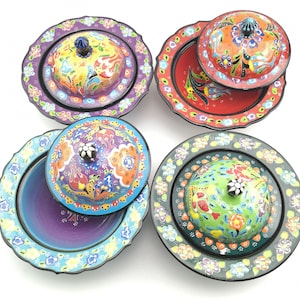 May include: Four colorful ceramic bowls with lids, each featuring a different floral pattern. The bowls are decorated with intricate details and vibrant colors, including red, blue, green, yellow, and purple.