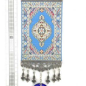 Puede incluir: Una alfombra con estampado azul y rojo colgada de un marco plateado con un amuleto de ojo turco azul colgando debajo.