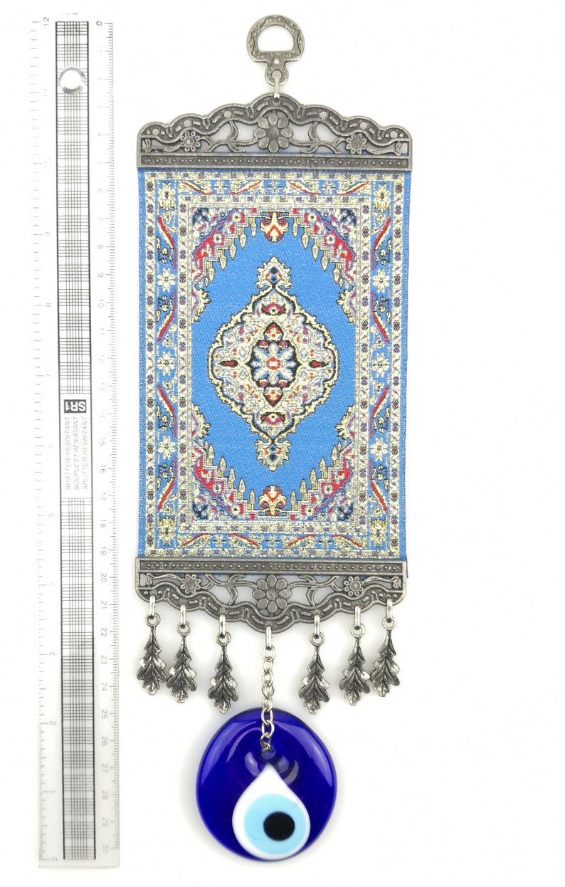 Puede incluir: Una alfombra con estampado azul y rojo colgada de un marco plateado con un amuleto de ojo turco azul colgando debajo.