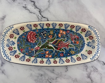 Könnte beinhalten: Eine ovale Servierplatte aus Keramik mit blauem Hintergrund und einem farbenfrohen Blumenmuster. Die Platte hat einen weißen Rand mit einem dunkelblauen Rand und roten und weißen Akzenten.