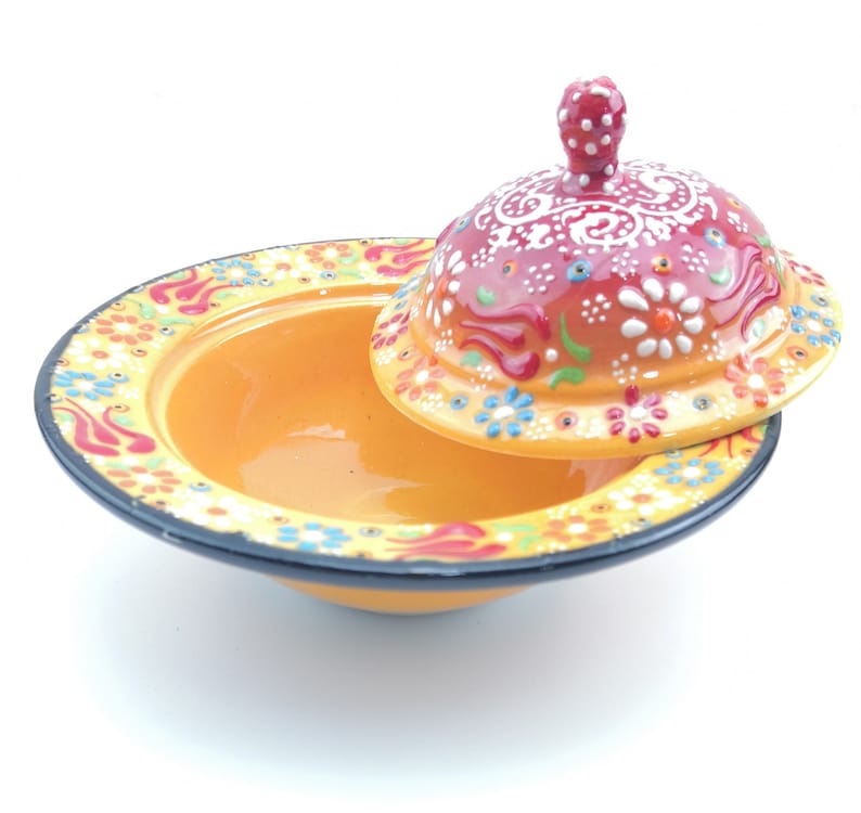 May include: A yellow ceramic bowl with a red and white floral design and a matching lid. The bowl is decorated with colourful flowers and swirls.