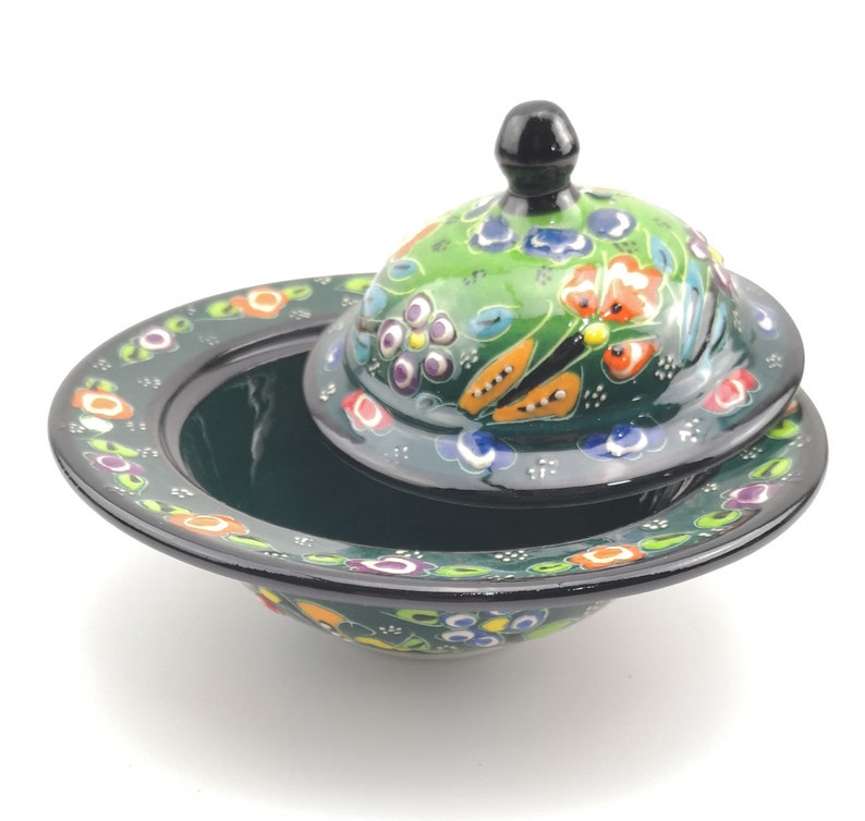 May include: A green ceramic bowl with a lid, both decorated with colourful floral patterns. The bowl has a wide rim and a slightly rounded base. The lid has a small knob on top.