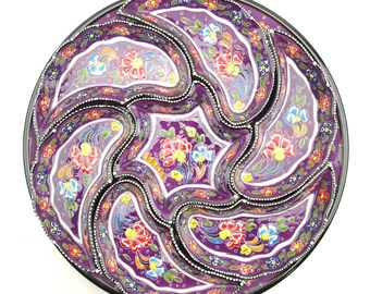 May include: A purple ceramic serving dish with six individual compartments. The dish is decorated with colorful floral patterns and a black rim.