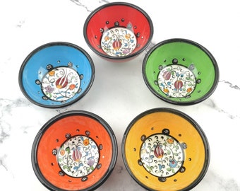 May include: Set of five small ceramic bowls with colorful floral designs. The bowls are red, blue, green, orange, and yellow. Each bowl has a black rim.