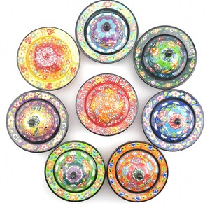 May include: Eight colourful ceramic bowls with lids, each featuring a different floral design. The bowls are arranged in a circle on a white background.