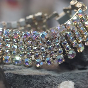 May include: A gold-toned bracelet with multiple rows of iridescent rhinestones. The bracelet is made of metal and has a clasp closure.