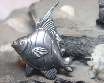 May include: A silver fish brooch with detailed scales and fins. The fish is facing to the right and has a slightly upturned mouth.