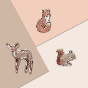 Könnte beinhalten: Drei gestickte Bügelbilder mit einem Fuchs, einem Reh und einem Eichhörnchen. Die Patches sind braun und weiß und eignen sich perfekt, um Kleidung oder Accessoires mit einem Hauch von Verspieltheit zu versehen.