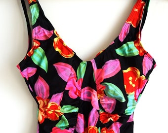 Pode incluir: Fato de banho preto de uma peça com um padrão floral vibrante. O fato de banho apresenta um decote em V profundo e alças largas. O design floral inclui flores e folhas rosa, vermelhas e verdes.