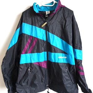 May include: Black Adidas track jacket with turquoise and purple accents. The jacket has a full zipper, a hood, and the Adidas logo on the chest. A vintage athletic jacket.
