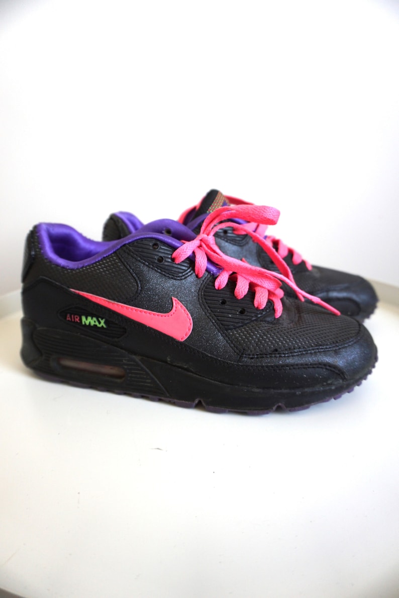 May include: Black Nike Air Max sneakers with pink laces and a purple trim. The Nike swoosh is pink.