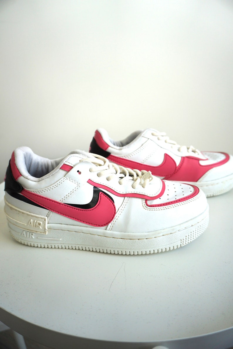 Puede incluir: Zapatillas blancas y rosas con detalles en negro. Las zapatillas presentan un logotipo y ribete rosa, con la marca "AIR" en la entresuela. Los cordones son blancos y el dise&ntilde;o es deportivo y moderno.