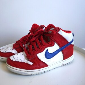 Puede incluir: Par de zapatillas altas rojas, blancas y azules. Las zapatillas tienen una parte superior de cuero rojo con detalles blancos en la puntera y el cuello. Un logotipo azul de la marca est&aacute; en el lateral. Cordones rojos.