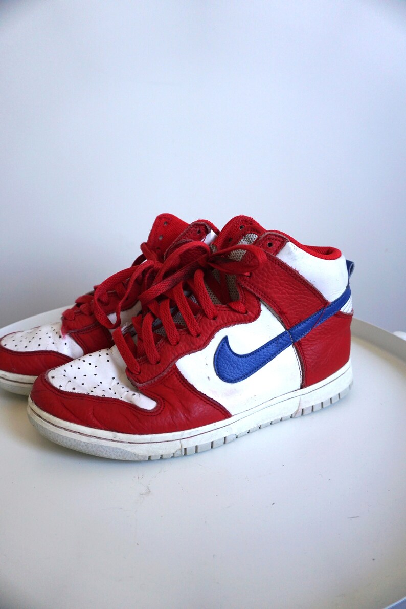 Puede incluir: Par de zapatillas altas rojas, blancas y azules. Las zapatillas tienen una parte superior de cuero rojo con detalles blancos en la puntera y el cuello. Un logotipo azul de la marca est&aacute; en el lateral. Cordones rojos.