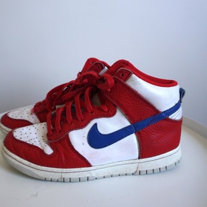 Puede incluir: Zapatillas altas rojas, blancas y azules con la parte superior de cuero. Las zapatillas deportivas presentan una entresuela blanca, cordones rojos y un logotipo azul en el lateral. Estilo atl&eacute;tico cl&aacute;sico.