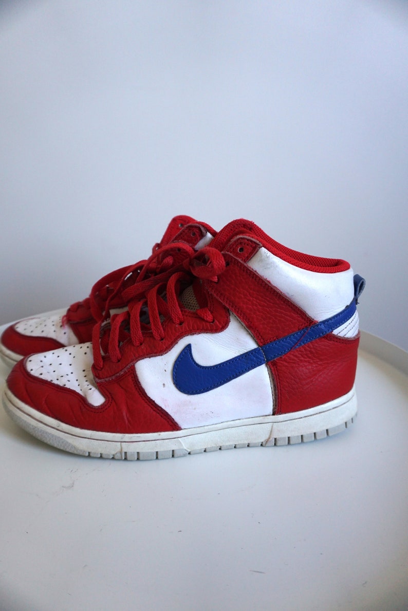 Puede incluir: Zapatillas altas rojas, blancas y azules con la parte superior de cuero. Las zapatillas deportivas presentan una entresuela blanca, cordones rojos y un logotipo azul en el lateral. Estilo atl&eacute;tico cl&aacute;sico.