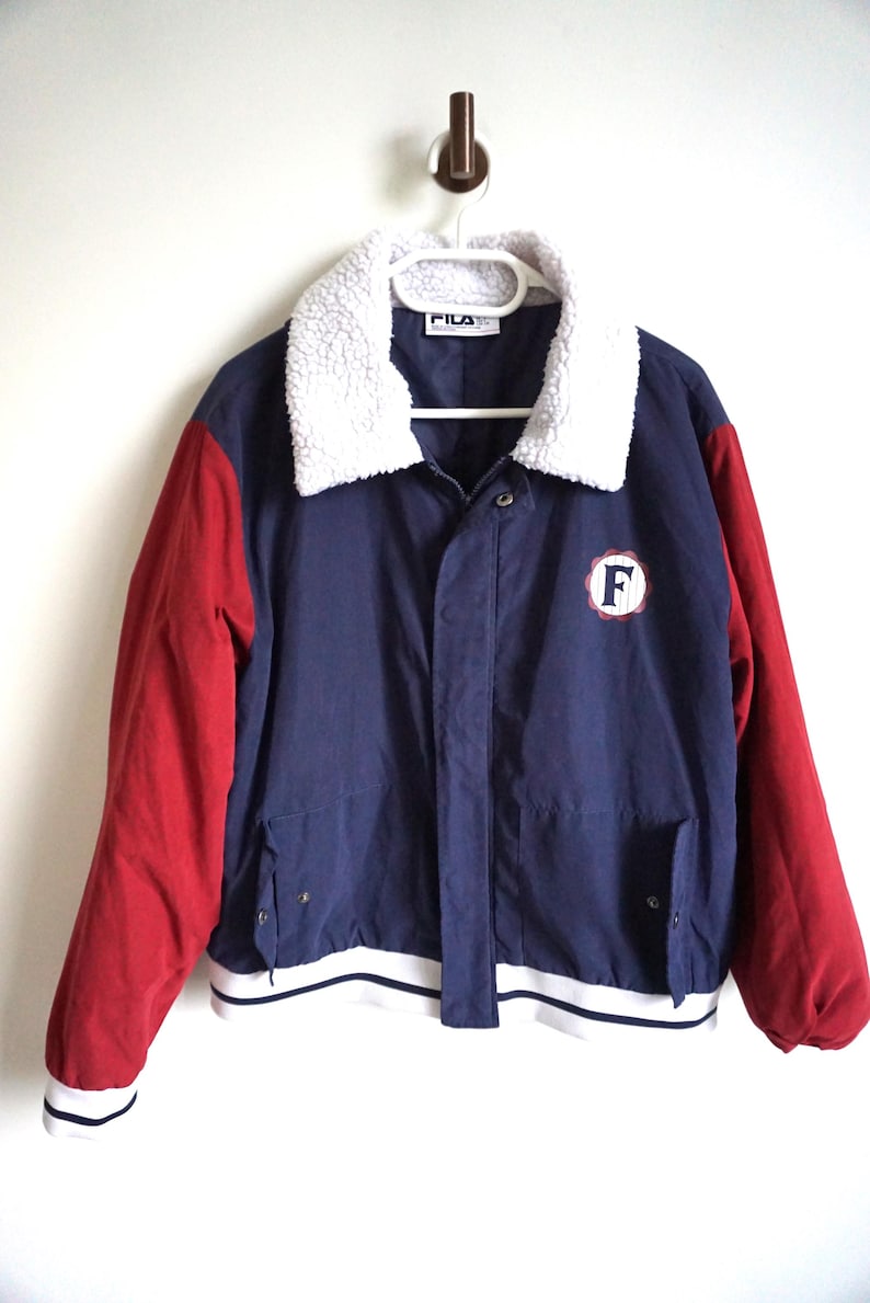 K&ouml;nnte beinhalten: Eine marineblaue und rote Vintage-Jacke mit wei&szlig;em Kunstfellkragen. Die Jacke hat rote &Auml;rmel, einen marineblauen K&ouml;rper und einen wei&szlig;en Streifen am Saum. Ein kreisf&ouml;rmiger Aufn&auml;her mit dem Buchstaben "F" befindet sich auf der Brust.