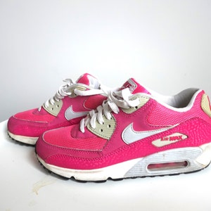 K&ouml;nnte beinhalten: Paar leuchtend pinkfarbene Air Max 90 Sneaker. Die Schuhe haben wei&szlig;e Schn&uuml;rsenkel, einen wei&szlig;en Nike-Swoosh und eine wei&szlig;e und graue Sohle. Die Worte "AIR MAX" sind auf der Seite des Schuhs zu sehen.