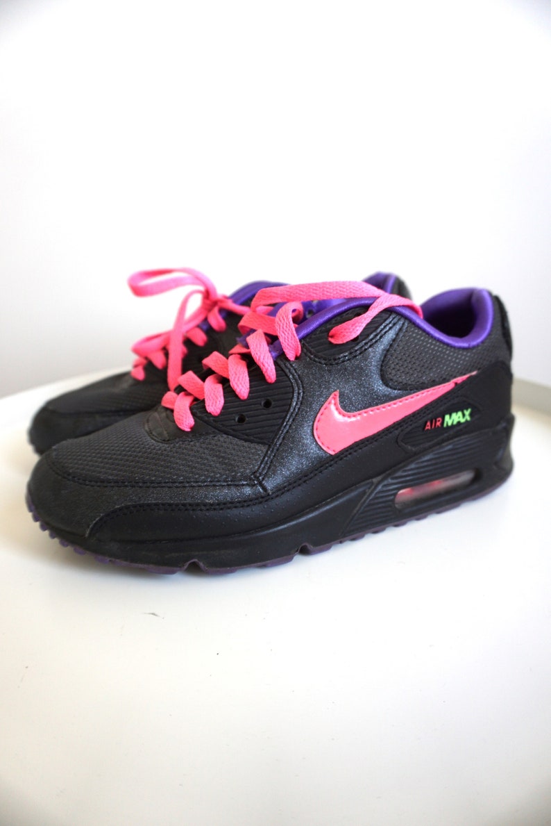 May include: Black sneakers with pink laces and a pink Nike swoosh. The sneakers have a purple trim and the text "AIR MAX" on the side.
