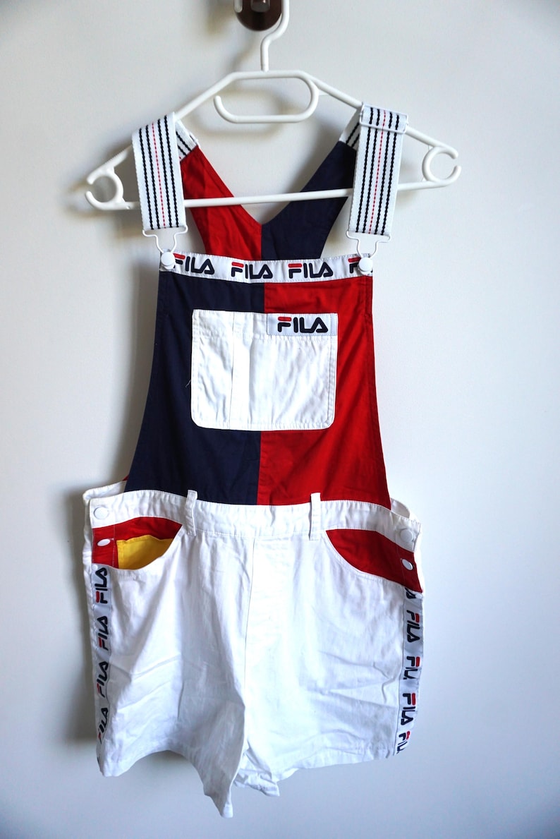 Puede incluir: Mono Fila vintage en blanco, azul marino y rojo. El mono con peto presenta un dise&ntilde;o de bloques de color con el logotipo de Fila en el bolsillo del peto y a lo largo del lateral del pantal&oacute;n corto. Las correas est&aacute;n rayadas con el logotipo de Fila.
