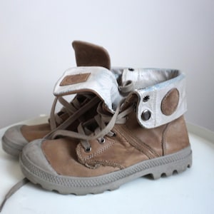 K&ouml;nnte beinhalten: Ein Paar hellbraune Lederstiefel mit grauer Gummi-Zehenkappe und Sohle. Die Stiefel haben einen umklappbaren Kragen mit hellgrauem und braunem Akzent. Die Schn&uuml;rsenkel sind hellbraun.