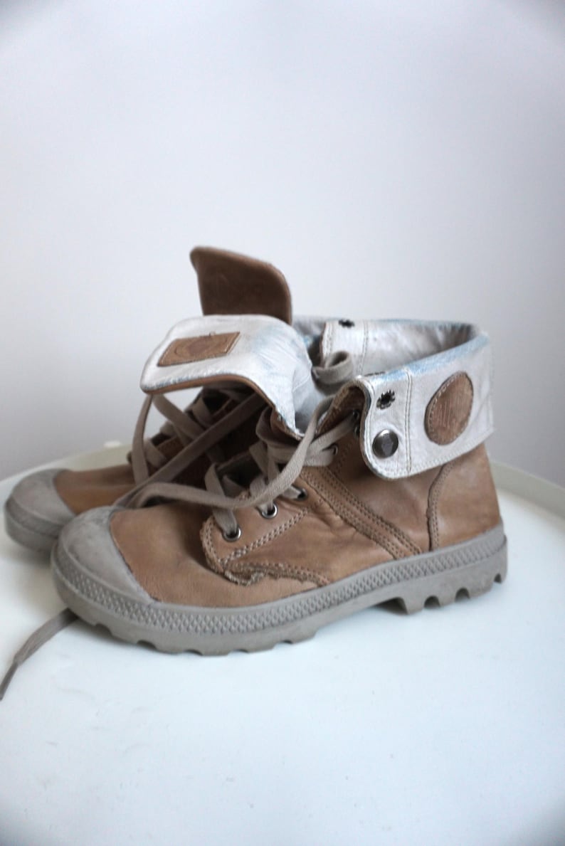 K&ouml;nnte beinhalten: Ein Paar hellbraune Lederstiefel mit grauer Gummi-Zehenkappe und Sohle. Die Stiefel haben einen umklappbaren Kragen mit hellgrauem und braunem Akzent. Die Schn&uuml;rsenkel sind hellbraun.