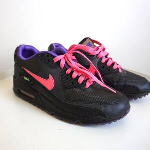 May include: Black Nike Air Max 90 sneakers with pink laces and a purple trim. The shoes have a mesh and leather upper and a white midsole.