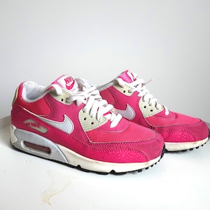 K&ouml;nnte beinhalten: Paar pinkfarbene Nike Air Max 90 Sneaker. Die Schuhe haben wei&szlig;e Schn&uuml;rsenkel, eine wei&szlig;e und graue Sohle und einen wei&szlig;en Nike Swoosh. Die Zunge des Schuhs hat das Nike Air Logo. Die Schuhe stehen auf einer wei&szlig;en Oberfl&auml;che.