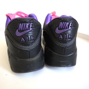 May include: A pair of black Nike Air Max sneakers with purple and pink accents. The back of the shoes feature the Nike logo and "Air" text in purple.