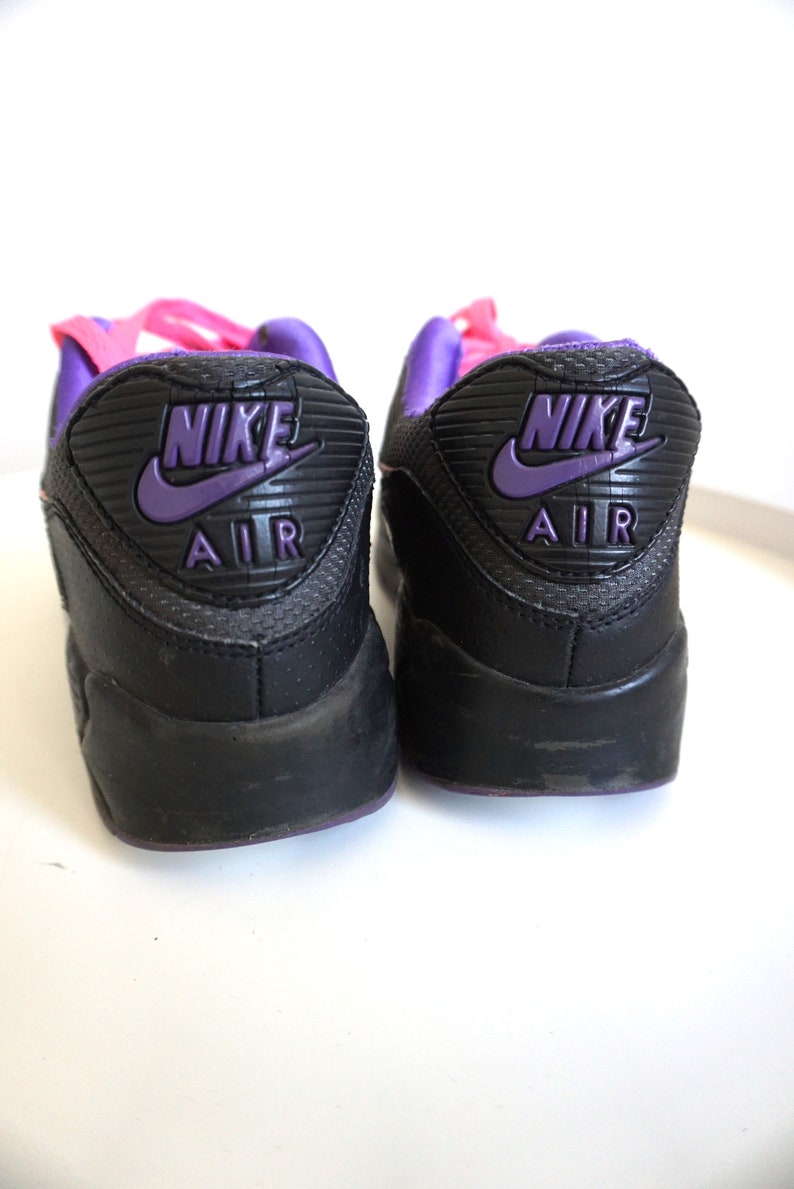 May include: A pair of black Nike Air Max sneakers with purple and pink accents. The back of the shoes feature the Nike logo and "Air" text in purple.
