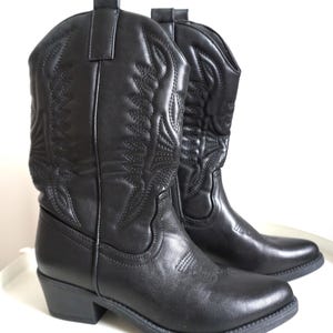 May include: A pair of black cowboy boots. The boots feature decorative stitching and a pointed toe. They are made of a smooth material and have a low heel. The boots are approximately 30 cm tall.