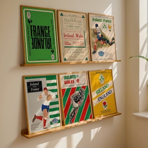 May include: A collection of framed vintage rugby posters displayed on wooden shelves. The posters feature vibrant colors and text, including "France Irlande" and "Ireland Wales." The posters are in wooden frames and are mounted on a white wall.