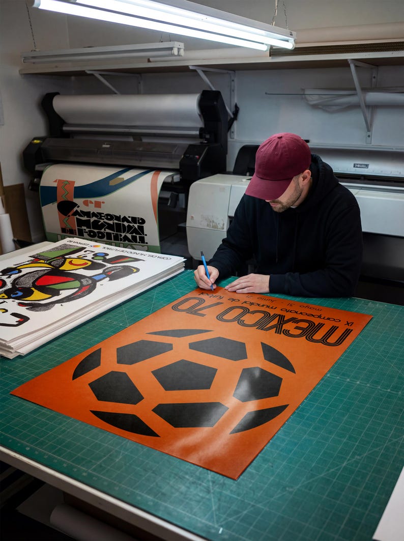 May include: A rectangular poster featuring a large black soccer ball graphic on an orange background with the text MEXICO 70 and IX campeonato mundial de futbol, mayo 31 - junio 21 printed in black ink on the lower portion of the paper sheet.