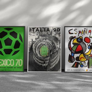 May include: Three framed posters featuring soccer tournament art. The left poster is green with a black soccer ball and text reading MEXICO 70. The center poster shows a stadium with ITALIA 90 text. The right poster features abstract art and ESPA&Ntilde;A 82 text.