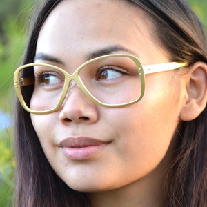 May include: A woman wearing gold-rimmed glasses with a square, rounded shape. The glasses have a light gold frame and clear lenses.