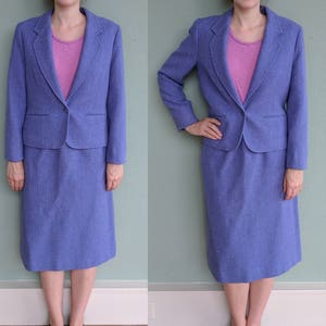 May include: A purple skirt suit with a matching blazer and skirt. The blazer has a single button closure and a notched collar. The skirt is knee-length and has a straight silhouette.