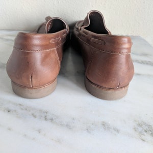 May include: A pair of brown leather loafers with a tassel detail. The loafers have a rubber sole and are shown from the back.